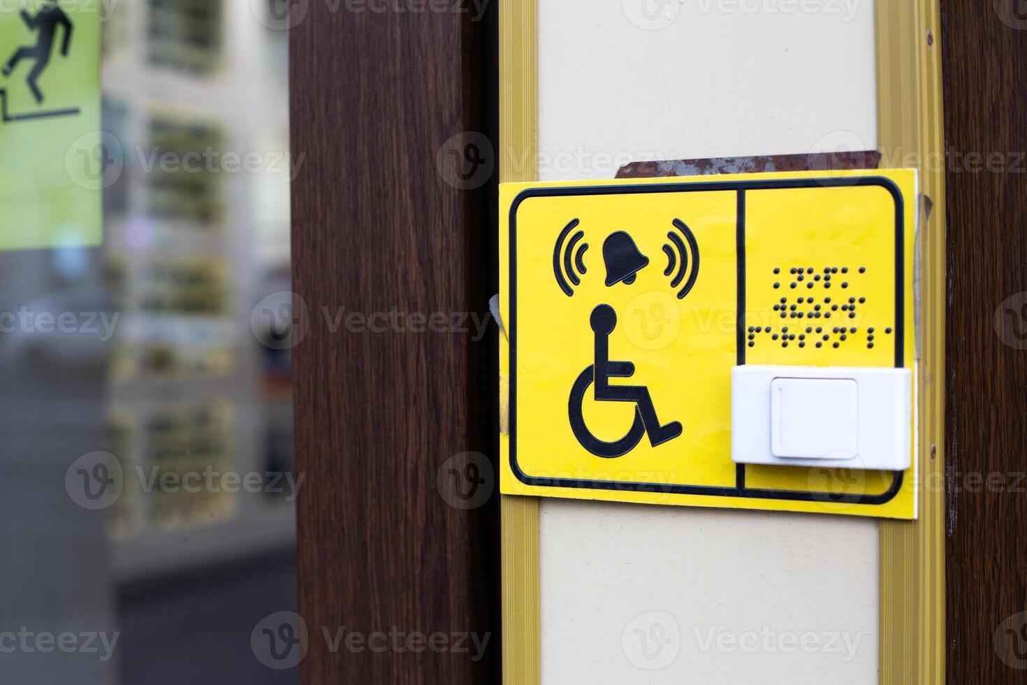 Building entrance is accessible for people with disabilities. Sign with braille text and symbol of person in wheelchair next to button to call assistant who will help you in entering building photo