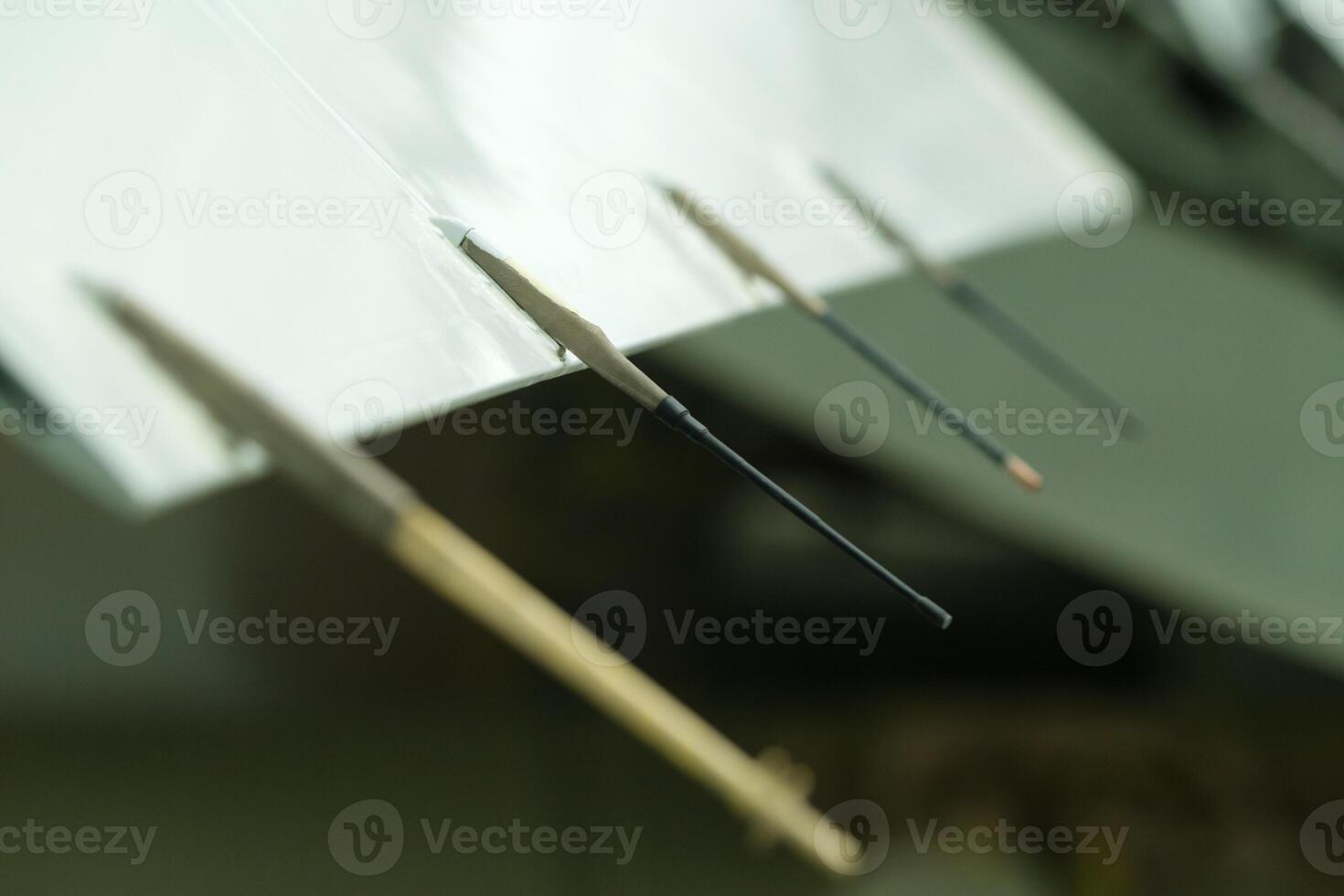 Paintbrushes in various sizes and shapes arranged artistically on a work surface in a creative studio, showcasing colorful tips that indicate active painting sessions and artistic expression photo