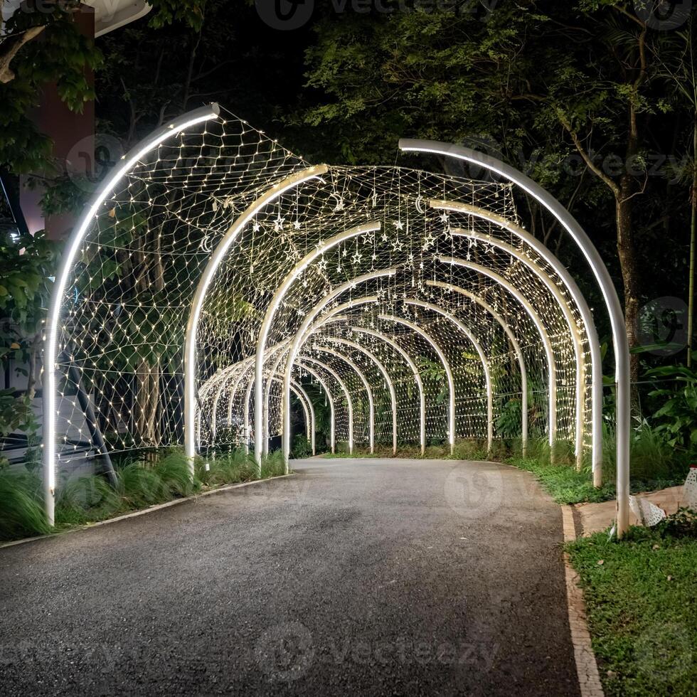 Curved white beams form an illuminated tunnel accented with hanging lights, and the structural lines create a clean pattern against the dark background.g photo