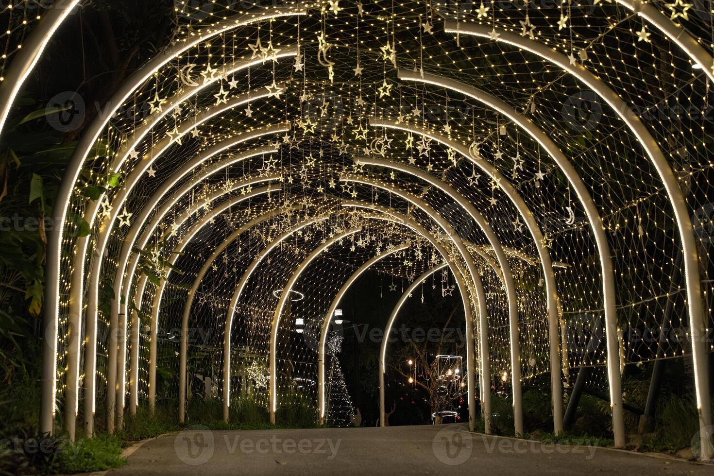 Curved white beams form an illuminated tunnel accented with hanging lights, and the structural lines create a clean pattern against the dark background.e photo