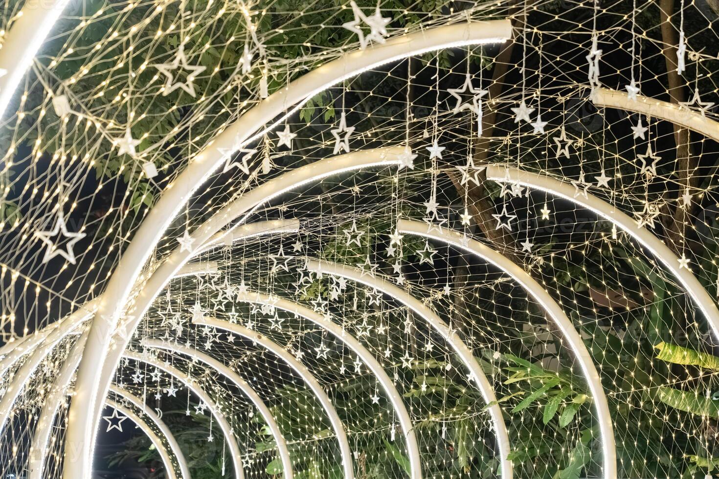 Curved white beams form an illuminated tunnel accented with hanging lights, and the structural lines create a clean pattern against the dark background.w photo