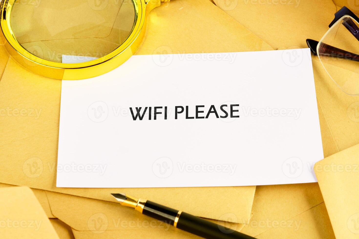 In a warm workspace, a note saying wifi please is placed among envelopes and a pen. A pair of glasses and a magnifying glass are nearby, adding to the inviting atmosphere photo