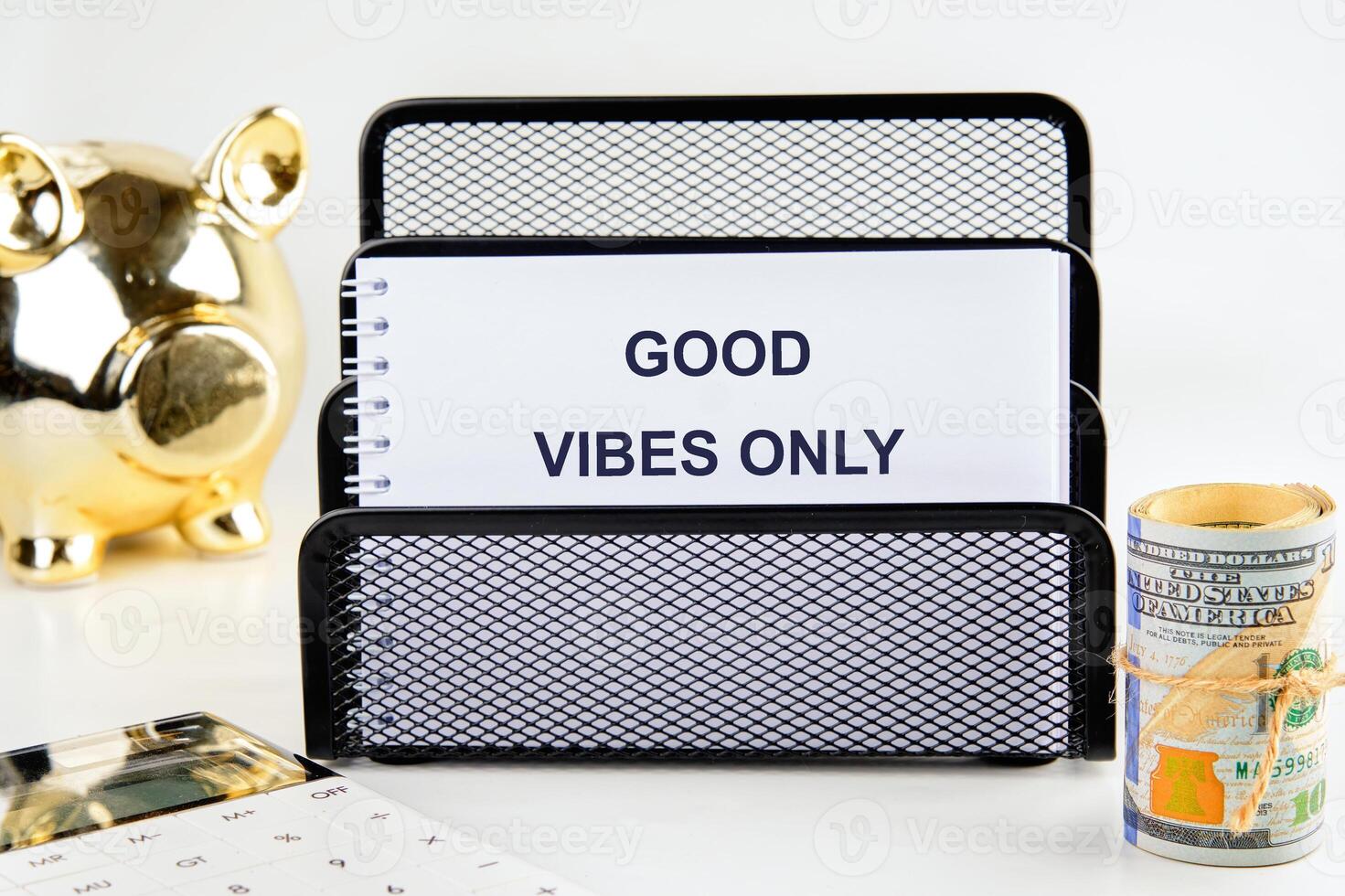 A creative workspace showcases a message of good vibes only. A piggy bank stands beside a notebook holding an uplifting reminder, encouraging a positive atmosphere for productivity photo