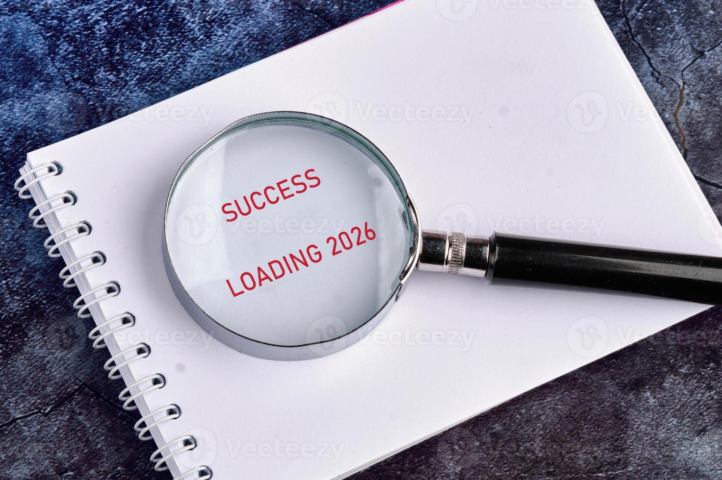 A notepad sits on a textured surface, showcasing a message of hope. A magnifying glass highlights the words SUCCESS LOADING 2026, symbolizing perseverance and future achievements photo