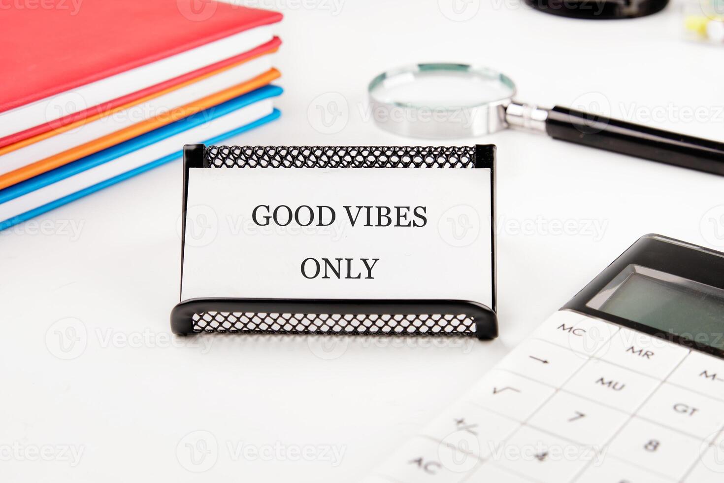 A desk displays the encouraging message GOOD VIBES ONLY, alongside colorful notebooks, a calculator, and a magnifying glass, creating an atmosphere of positivity and productivity photo