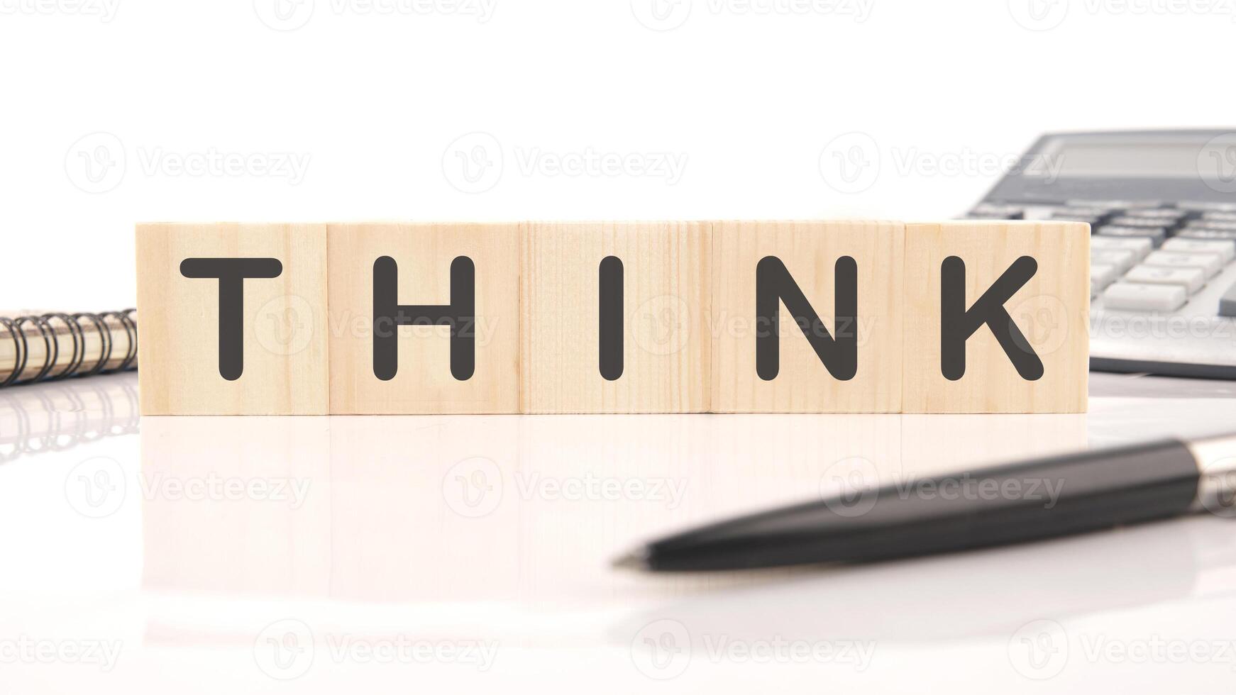 Wooden blocks spelling THINK sit on a white surface with a notepad, pen and calculator. The arrangement inspires creative brainstorming and problem-solving photo