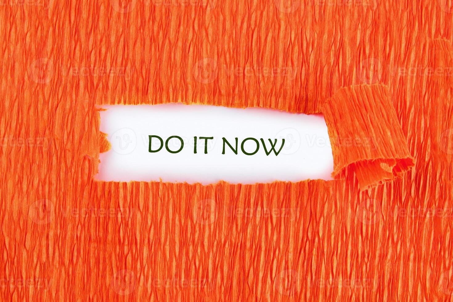 Orange crepe paper is torn to reveal Do It Now written in green on a white background, creating an immediate and urgent call to action photo