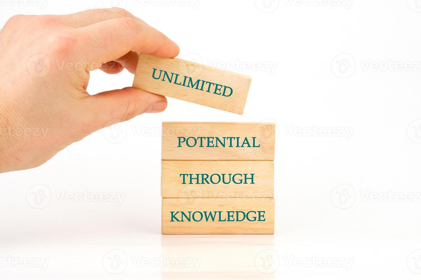 A hand carefully places a wooden block labeled unlimited on a stack of blocks that spell out potential through knowledge, symbolizing growth and learning photo