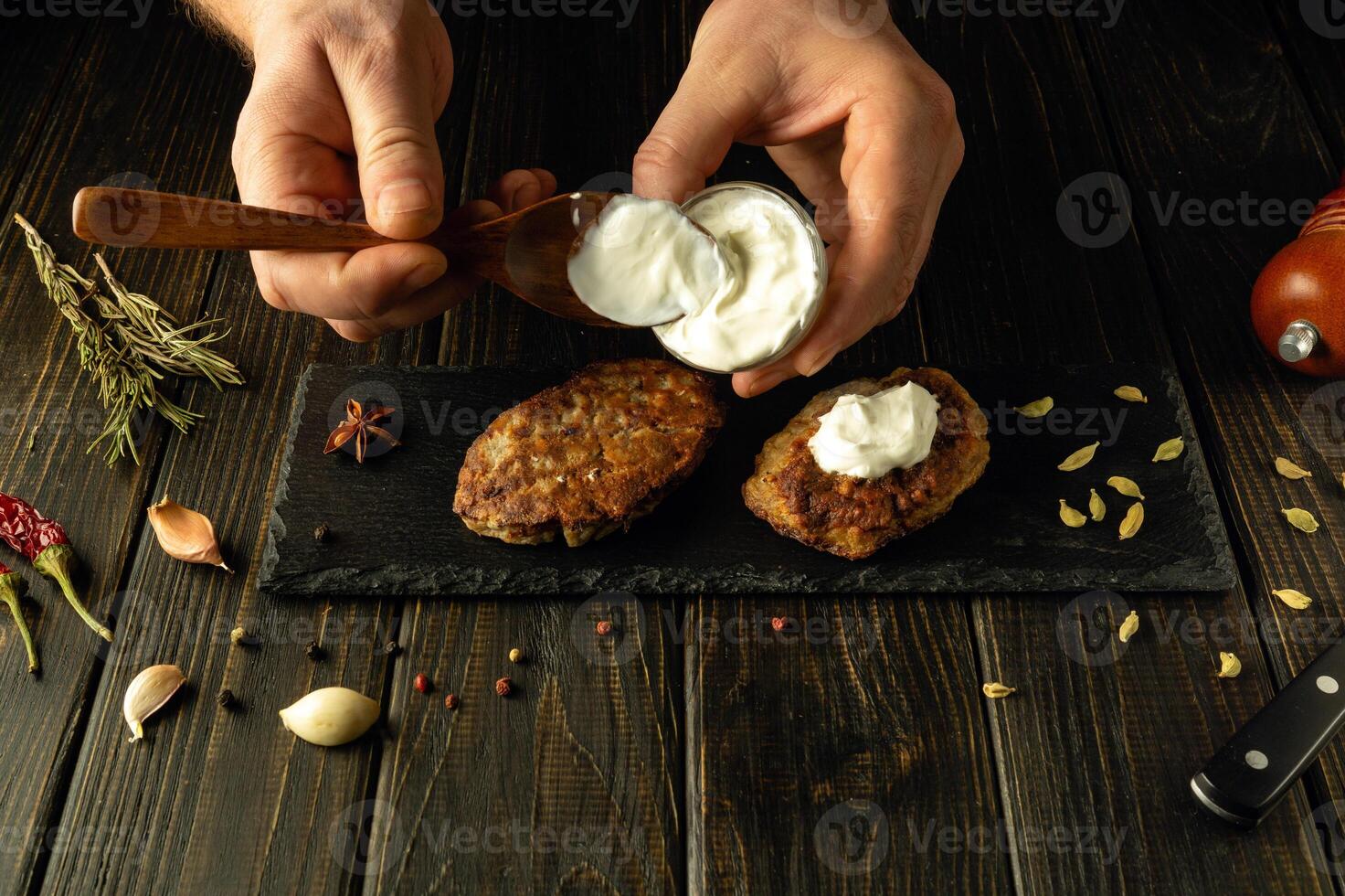 Close-up of a chef hands using a spoon adding sour cream to fried cutlets on a sorting board. The concept of preparing delicious food in a hotel photo