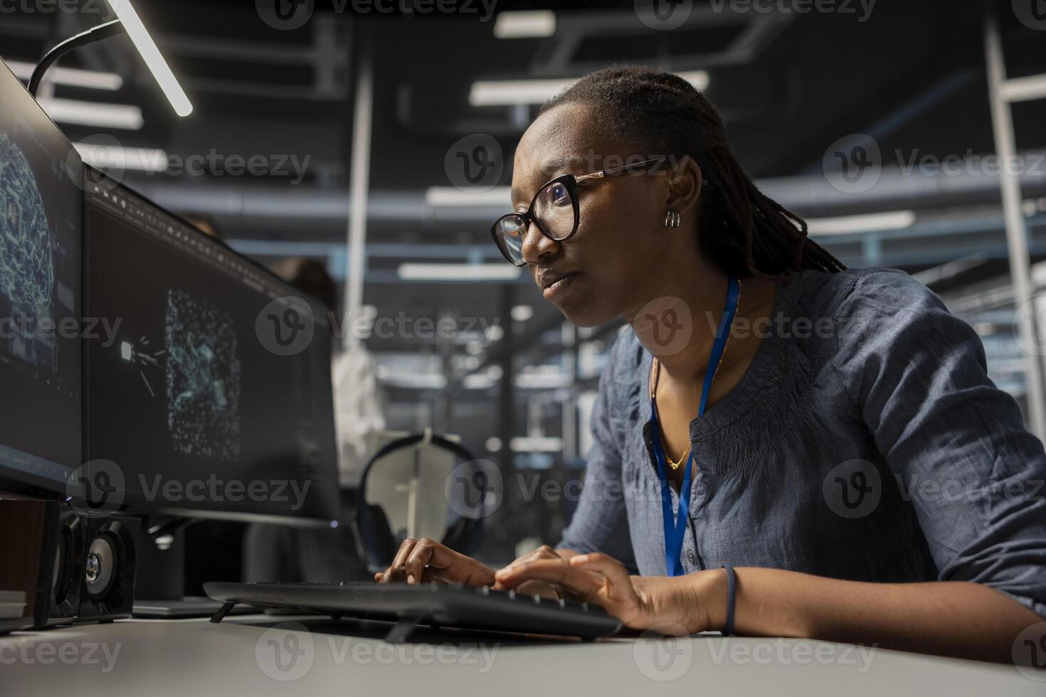 Focused data center developer using artificial intelligence deep learning tech. African american woman in server hub looking at AI programming language on PC monitor to update gear photo