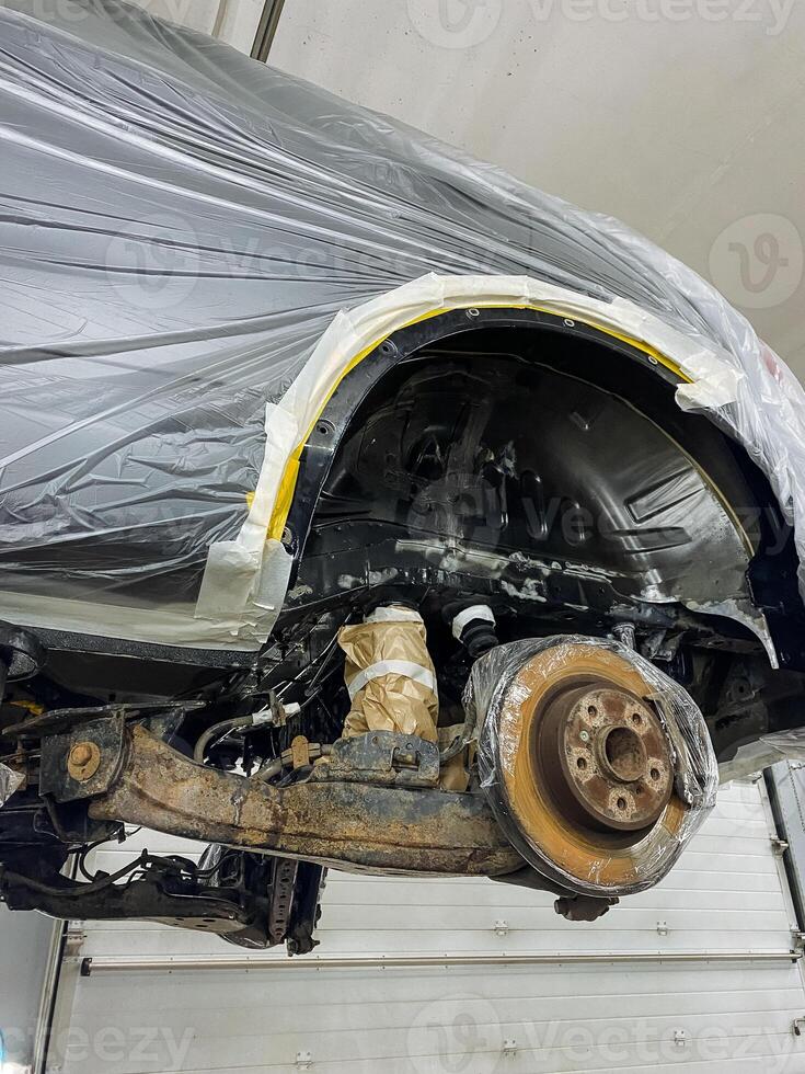 vehicle brake repair, rusty rotor and hub being repaired by technician in workshop setting, automotive service technician replacing brake components on lifted vehicle with visible rust and tools photo