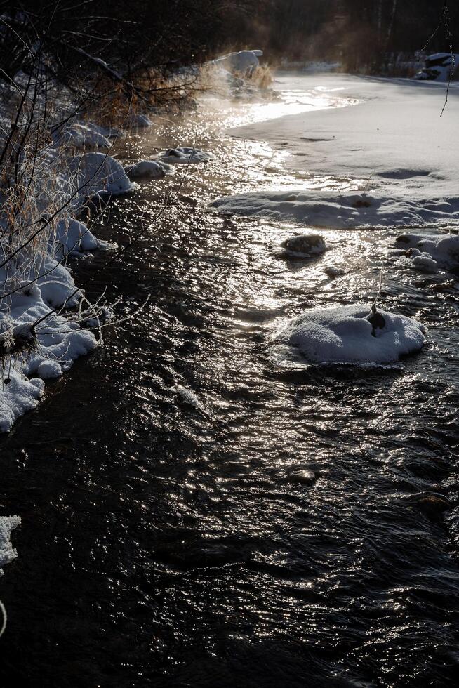 cold winter stream with ice, chilly winter rapids with floating ice and slippery stones surface, gloomy frozen stream rushing beneath stormy winter sky with icy patches and smooth stones photo