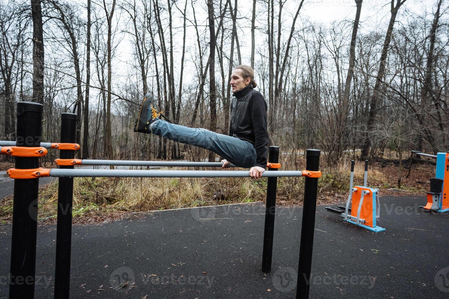 white athlete holding core hold on parallel bars, legs extended and torso steady, focused expression, bare park setting with leafcovered ground, impressive core strength and discipline photo