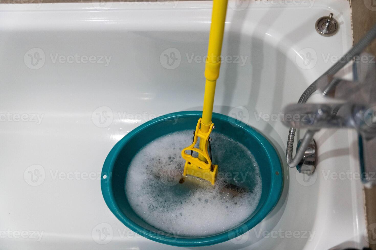 Cleaning tool submerged in a turquoise basin filled with soapy water, showcasing the process of maintaining hygiene in a bathroom environment with copy space photo