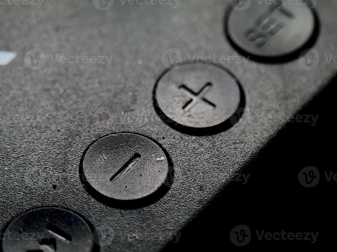 Textured black surface features round buttons with imprinted shapes, in dark and moody illumination. photo