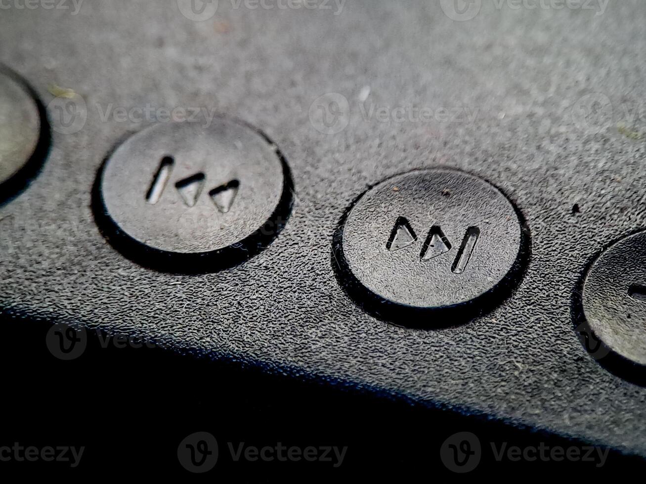 Textured black surface showcasing round buttons with symbol for rewind or fast forward action. photo