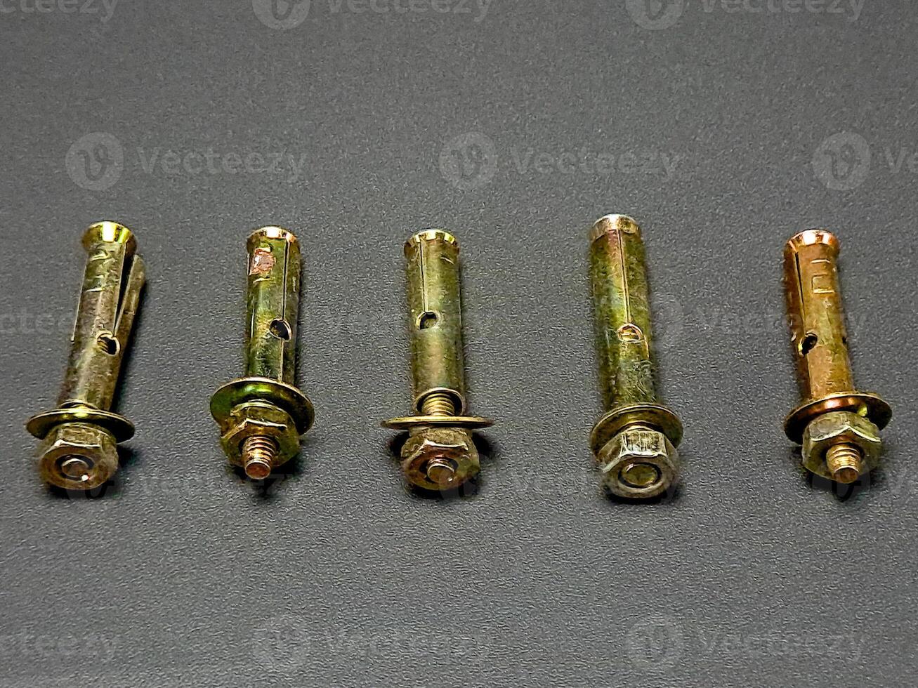 Five metal expansion bolts placed in a horizontal line on a textured gray surface, creating pattern. photo