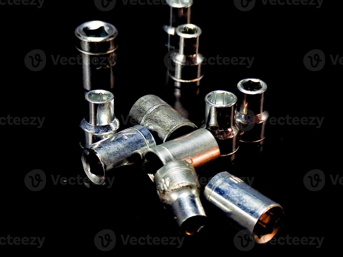 Symmetrical array of assorted metal sockets gleams dramatically on a stark black reflective plane. photo