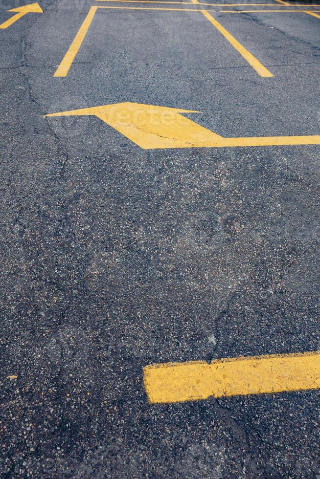 A close-up view of a parking lot surface with faded asphalt and yellow directional arrows. The ground shows wear and tear, indicating frequent use. photo
