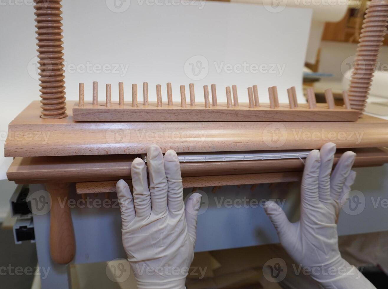 Gloved hands install a block of sheets in a wooden bookbinding press. Spine alignment, manual restoration, workshop. photo