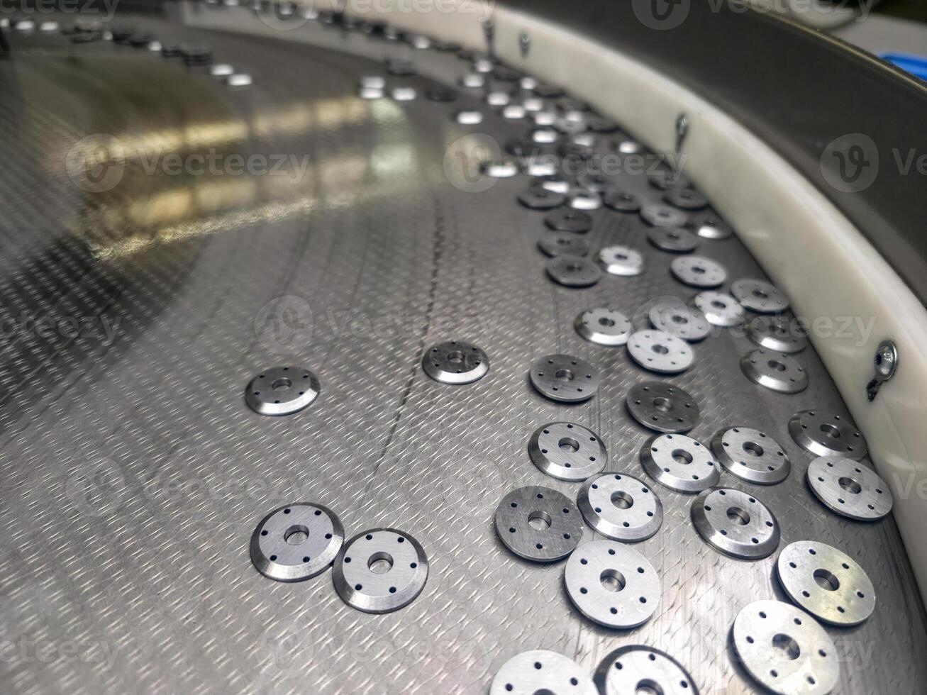 Shiny metal washers on an industrial sorting surface waiting for processing, a scene of mechanical repetition and automated precision photo