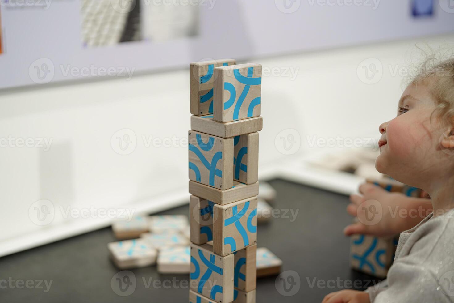 Child plays with wooden building blocks while creating a tall structure at an interactive learning exhibit in a museum photo