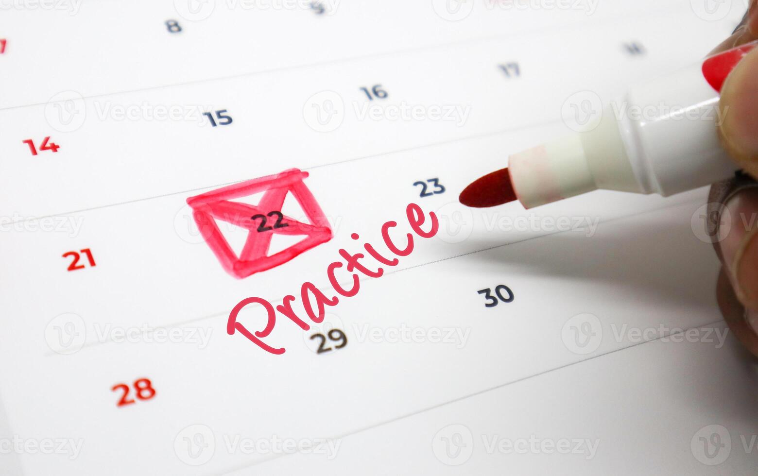 Hand marking Practice on a calendar date with a red marker, emphasizing important scheduling and event reminders photo