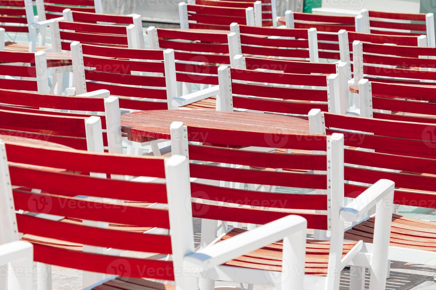Rows of red wooden chairs with white frames arranged outdoors in sunlight, backdrop as minimal style graphic pattern. Concept of order, repetition, structure and summer leisure. photo