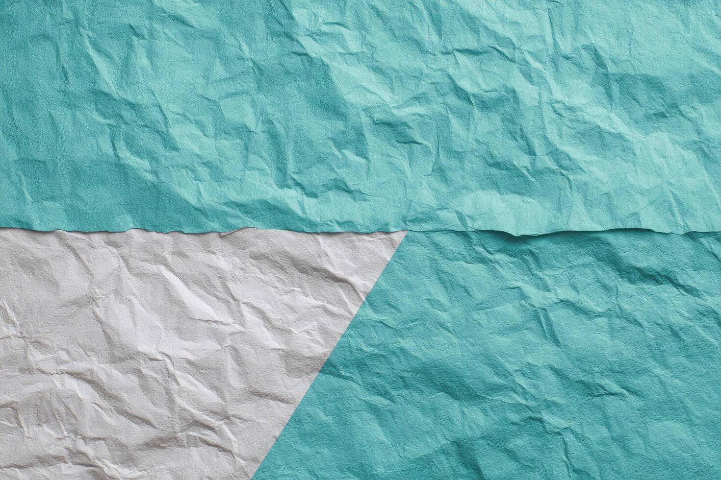 Crumpled paper background showcasing two distinct tones of teal and white separated by a sharp diagonal line. photo