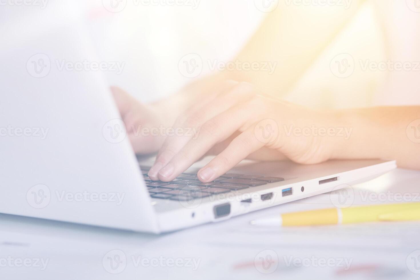 Woman's hands typing on keyboard of notebook, sitting at table against white background, white lap top and yellow pen on desk, female working online via Internet, checking her e mail, has message. photo