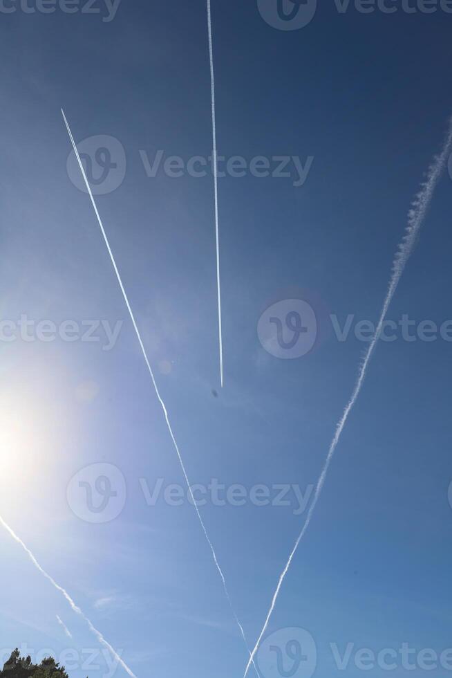 Contrails from aircraft create dynamic patterns in the clear blue sky, with sunlight illuminating the scene, showcasing the beauty of aviation and nature combined photo