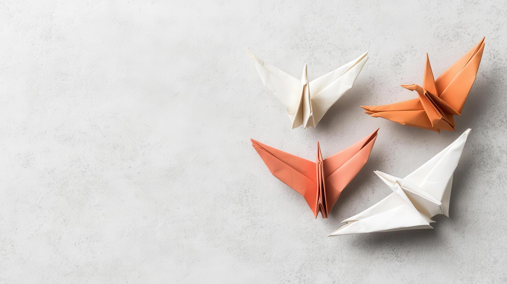Four paper cranes in soft orange and white sit on a textured light grey surface, symbolizing imaginative thought and graceful movement. photo