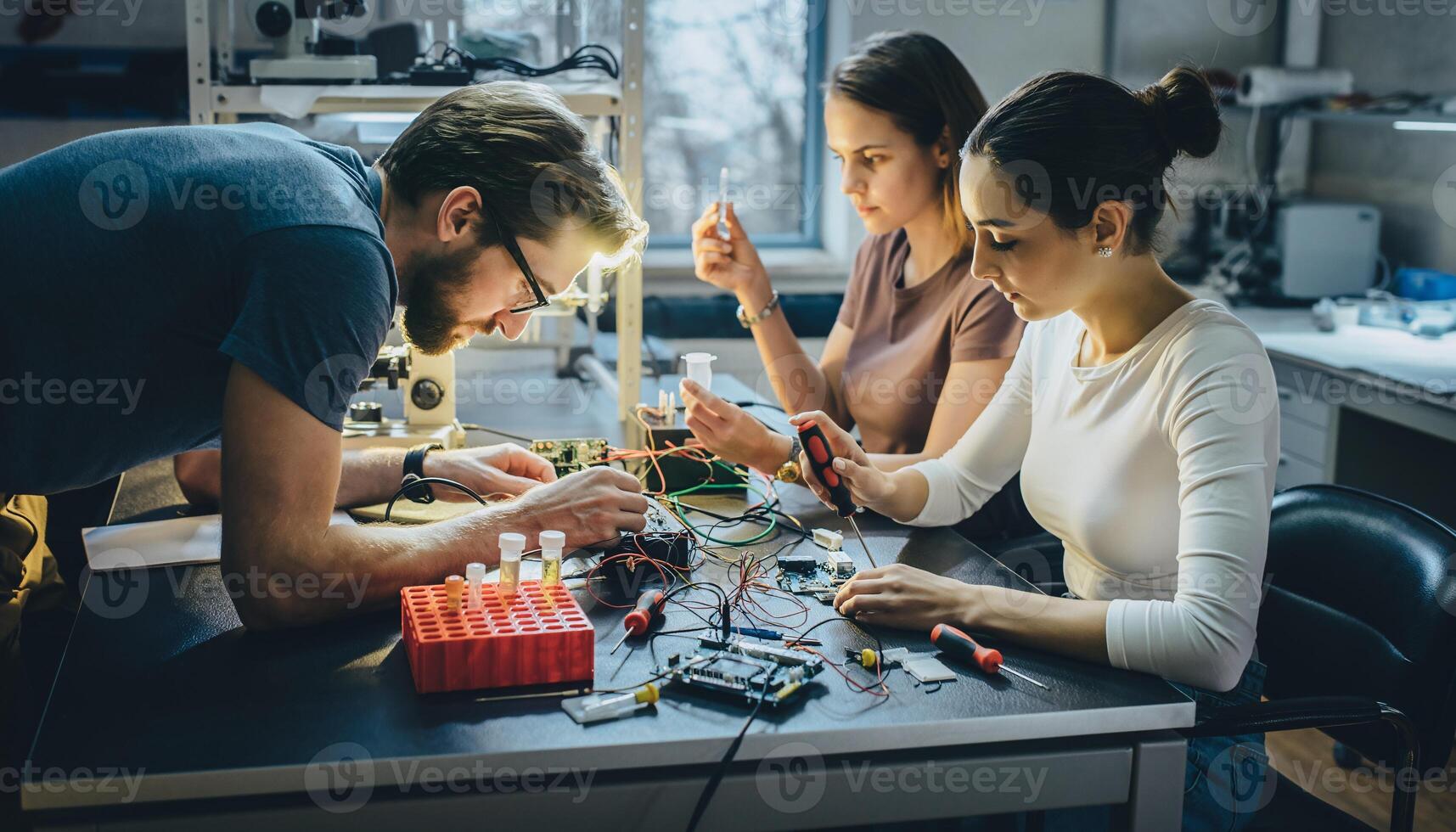 Diverse team of young engineers working on electronics project in modern lab setting developing technology innovation STEM education teamwork photo