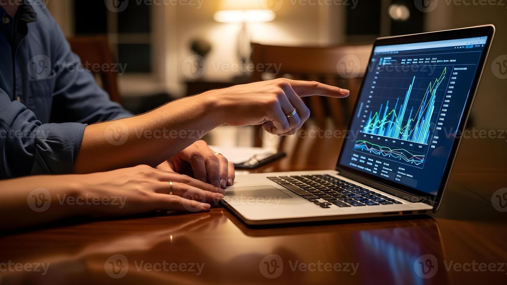 A person points to a graph on a laptop screen while working at a table. photo