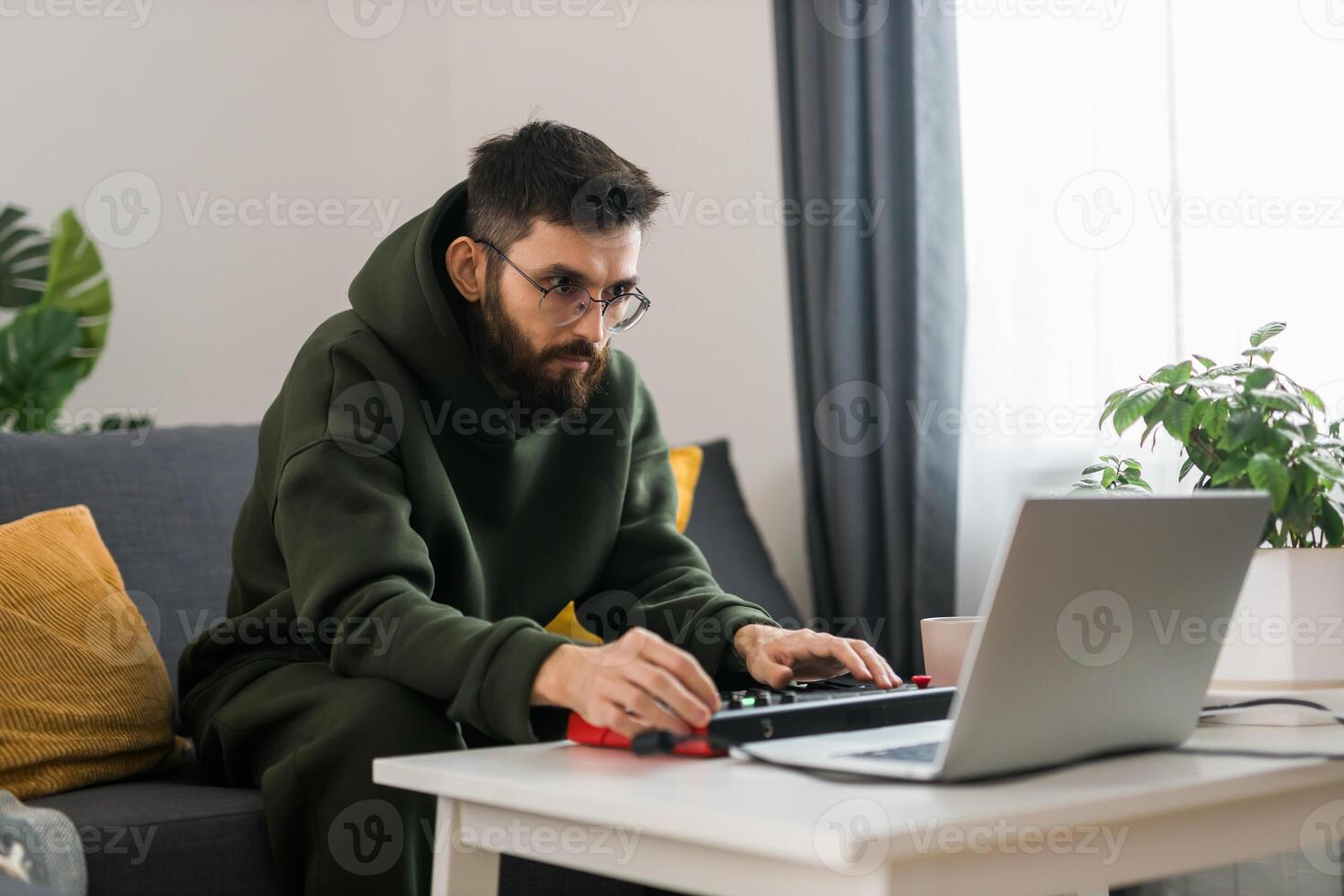 Man recording music track with portable midi keyboard on laptop computer in home studio. Producing and mixing music beat making and arranging audio content with professional audio devices close-up photo