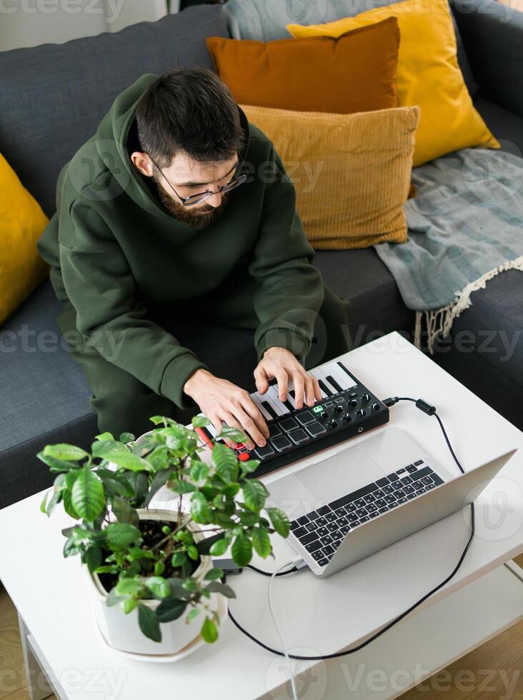Top view Man recording electronic music track with portable midi keyboard on laptop computer in home studio. Producing and mixing music beat making and arranging audio content. photo