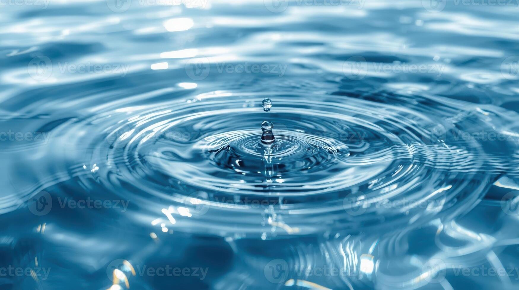 A single water droplet creates concentric ripples expanding across a surface of clear blue water in an abstract macro liquid motion scene. photo