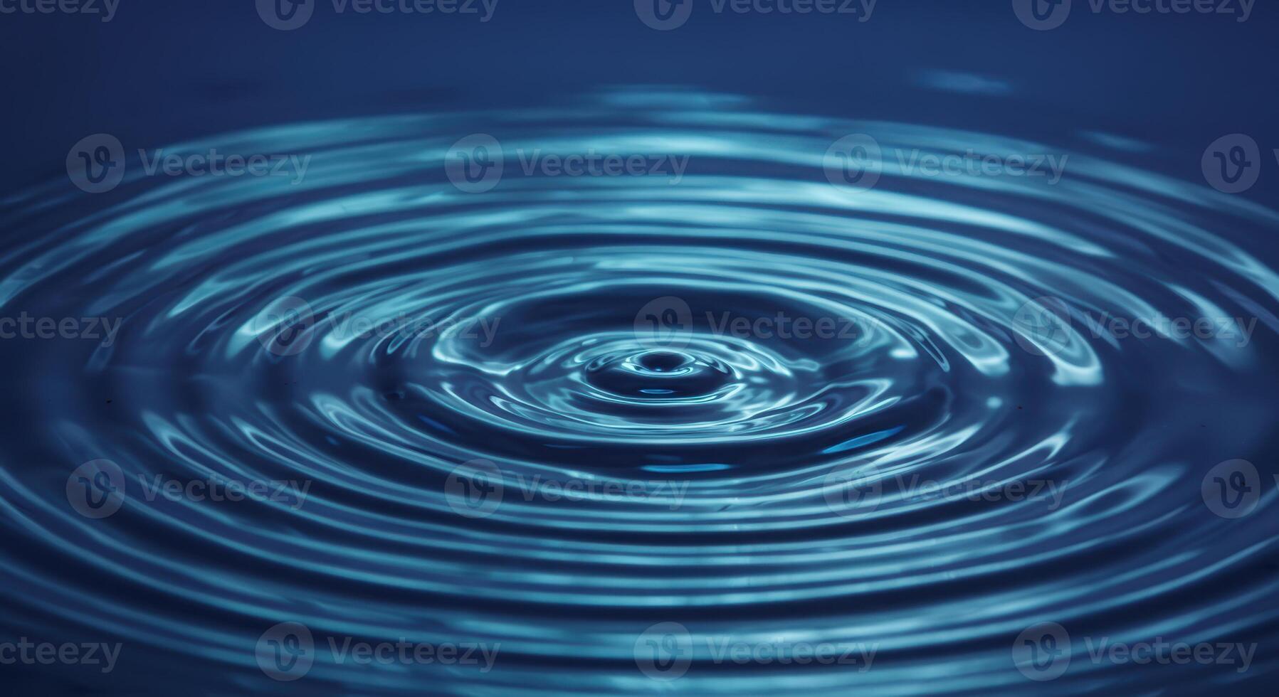 A single drop of water creates concentric circular ripples on the deep blue surface of a calm liquid forming a beautiful pattern. photo