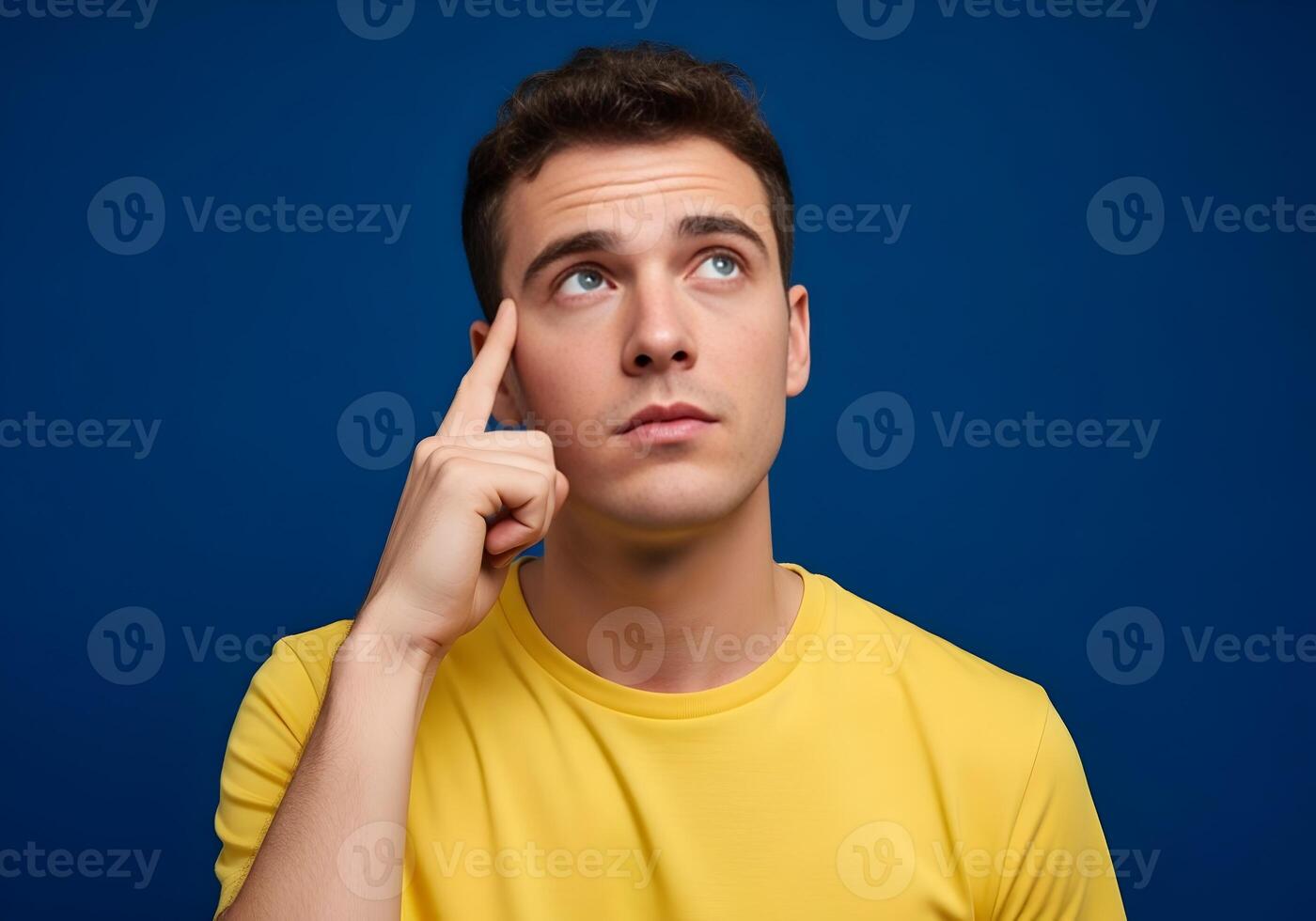 Young man deep in thought contemplating options and ideas for future projects looking up against a solid blue background symbolizing imagination and creative problem solving photo