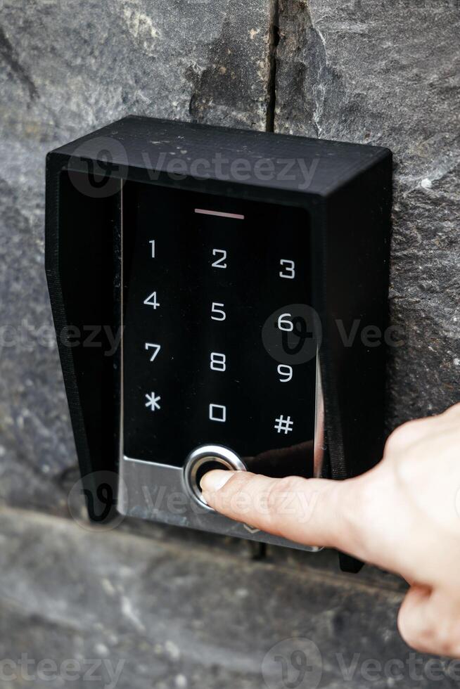 Modern digital keypad with a sleek design, featuring a user pressing the button, set against a textured stone wall, illustrating advanced security technology and convenience photo