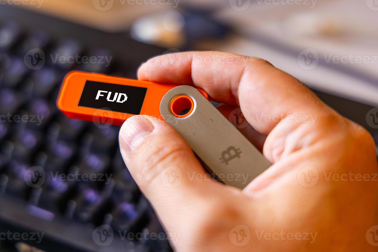 hardware Bitcoin wallet held in white hand with FUD message on screen photo