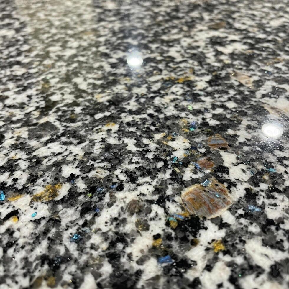 Close up view of a speckled granite countertop with a reflective surface showing subtle light glints and varied mineral patterns photo