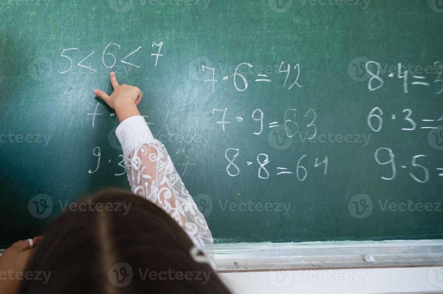 Child points to math problems on a green chalkboard, showcasing classroom learning and mathematical concepts being taught in the learning environment. photo