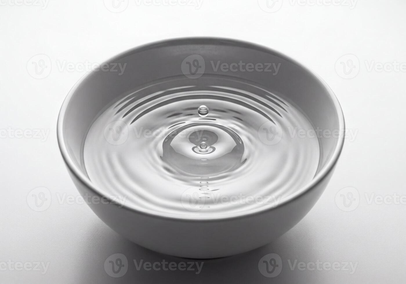 Dynamic moment of a water drop impacting a still surface in a bowl, creating ripples photo