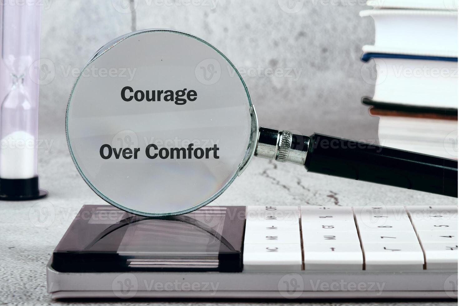 A motivational display emphasizes the phrase Courage Over Comfort through a magnifying glass on a flat surface. Books and a timer add to the productive atmosphere photo
