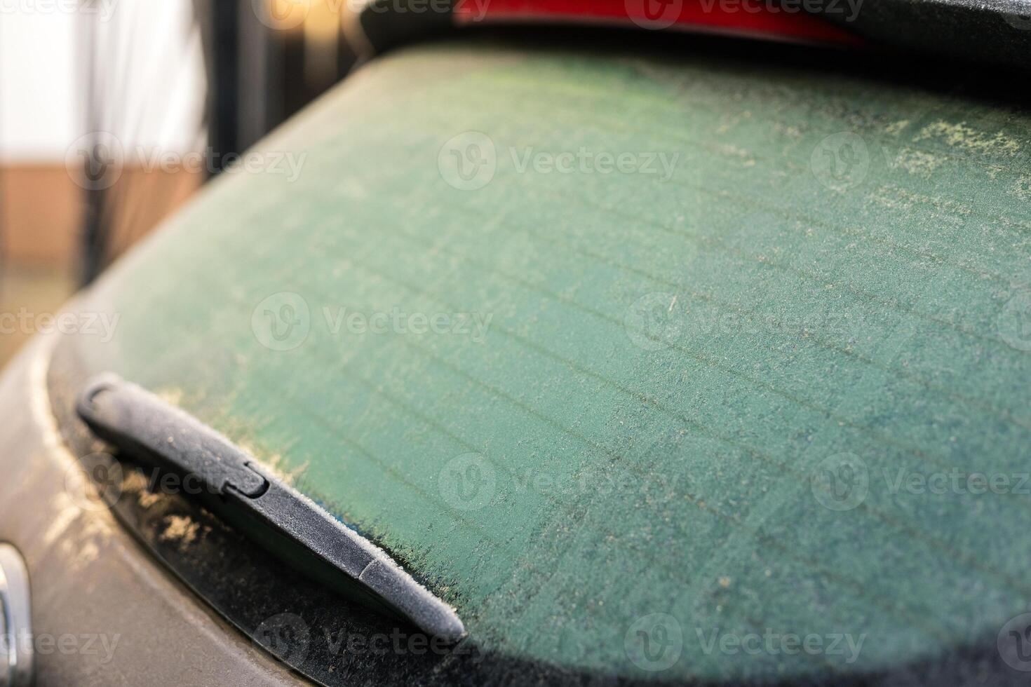 A car's windshield is covered in a layer of frost, showing early signs of winter. The soft light highlights the icy patterns, creating a chilly but beautiful scene photo