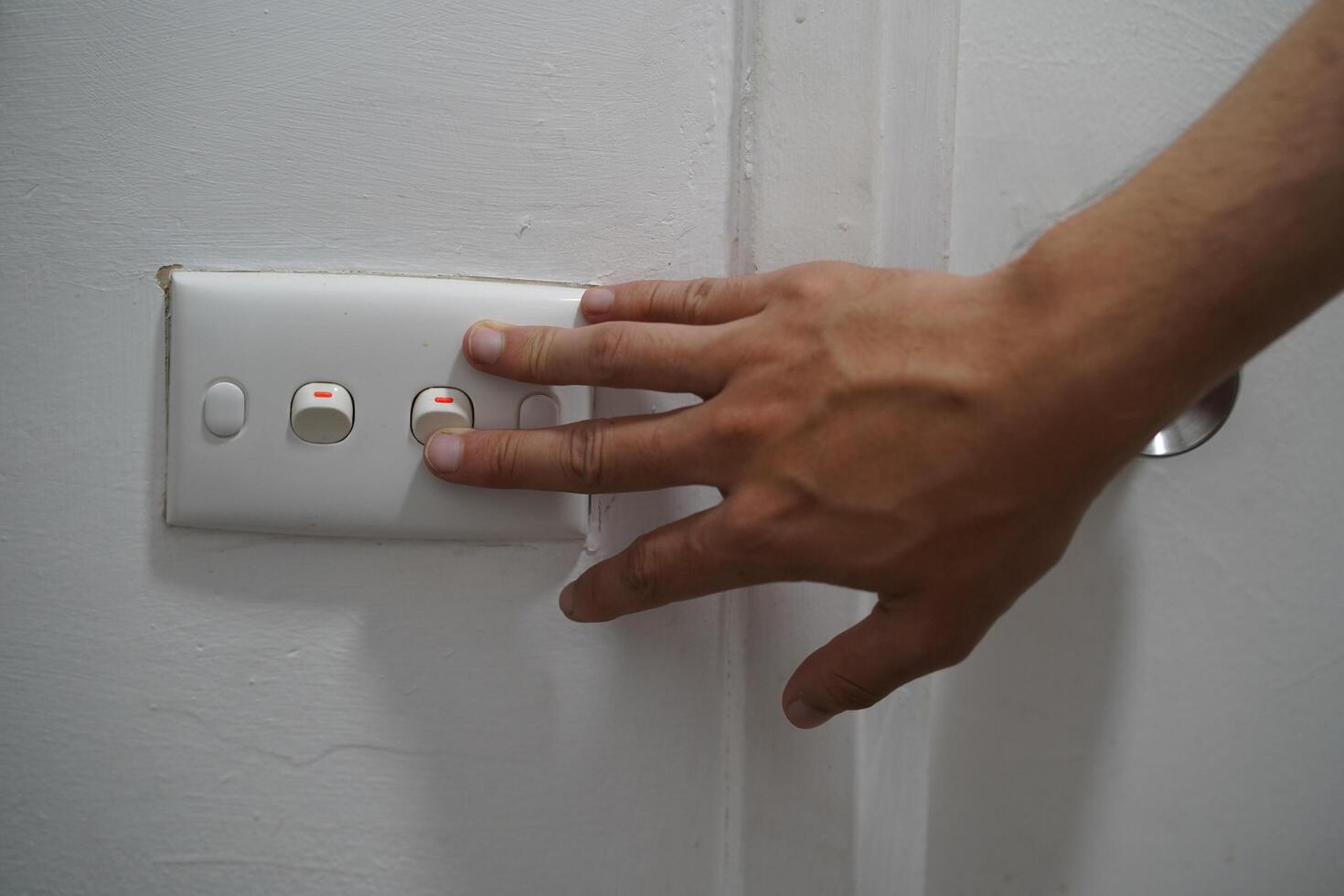 Hand Reaching Toward Light Switch on White Wall with Three Buttons for Controlling Lighting in Home Environment or Office Setting photo