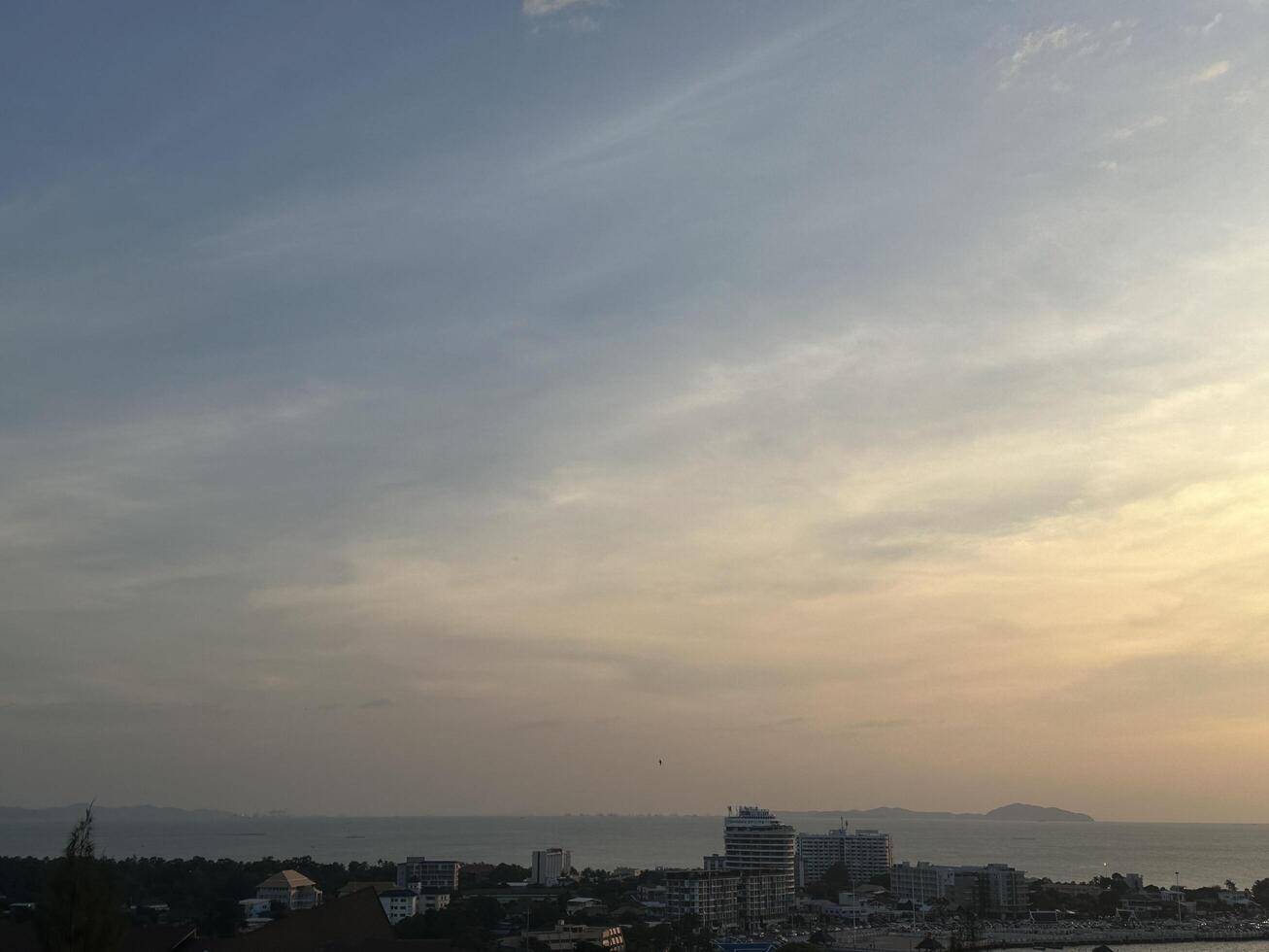 Serene Coastal Skyline at Dusk with Soft Clouds Over Tranquil Waters and Urban Development in the Foreground Illuminated by Fading Evening Light photo