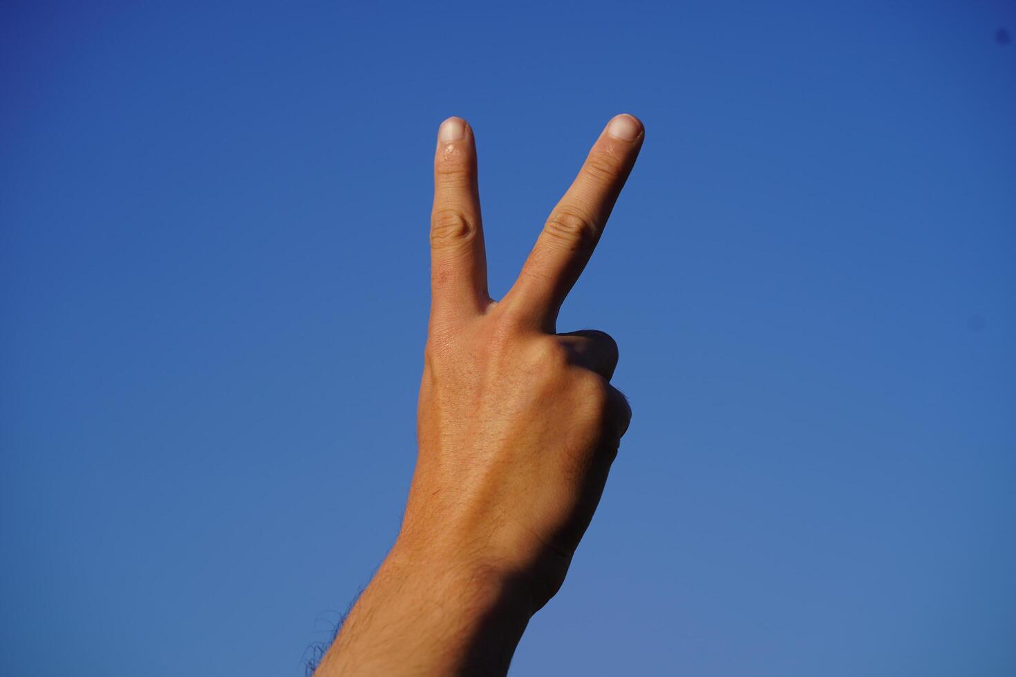 Hand gesture symbolizing peace against a clear blue sky showcasing unity, hope, and positivity in a vibrant and serene setting without distractions photo