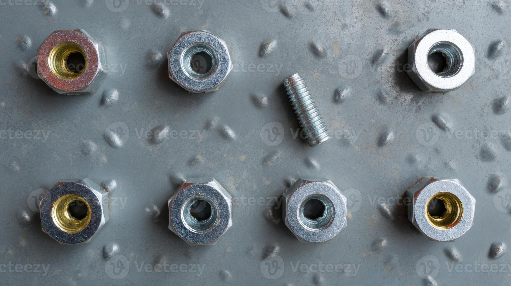 A close-up view of assorted nuts and a bolt on a textured metal surface, showcasing metallic textures and shapes. photo
